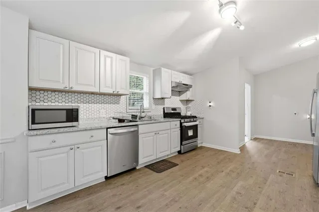 a kitchen with stainless steel appliances granite countertop a refrigerator a sink dishwasher a stove and white countertops with wooden floor