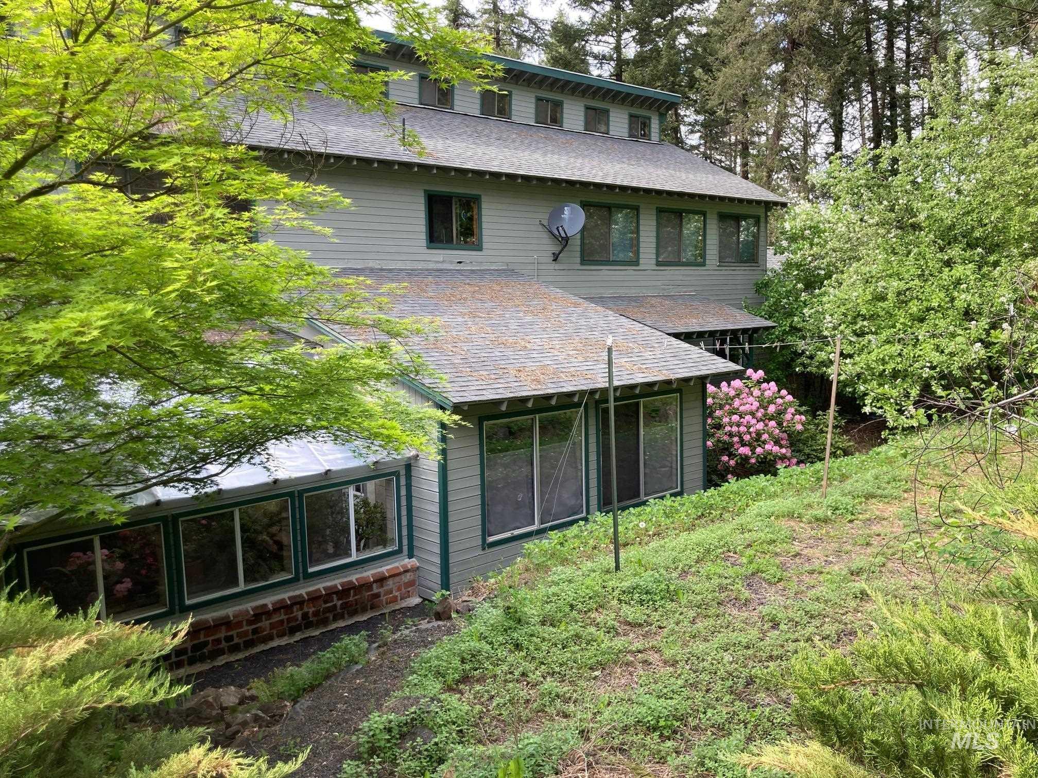 266 Falcon Ridge Road Kooskia, ID 83539 - Photo 5 of 50 Multi-level residence featuring gray siding with green trim and a gabled roofline. Primary bedroom on main floor open to patio surrounded by strawberry beds and other fruits and flowers.