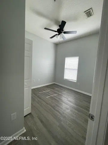 an empty room with wooden floor fan and windows