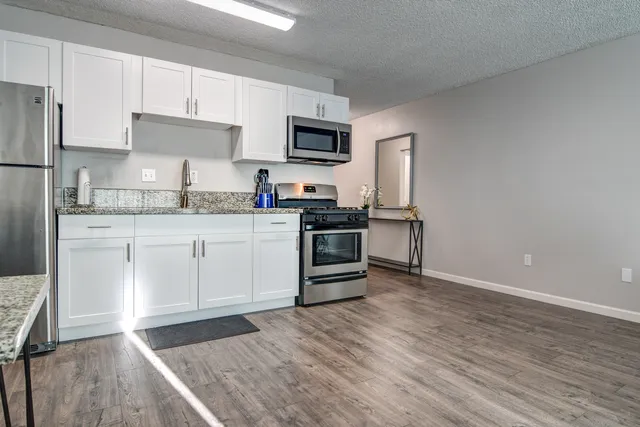 a kitchen with stainless steel appliances granite countertop a stove top oven a sink dishwasher and a refrigerator with wooden floor