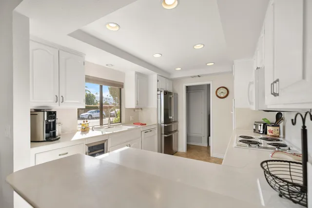 a large white kitchen with granite countertop a stove a sink a refrigerator and white cabinets with wooden floor