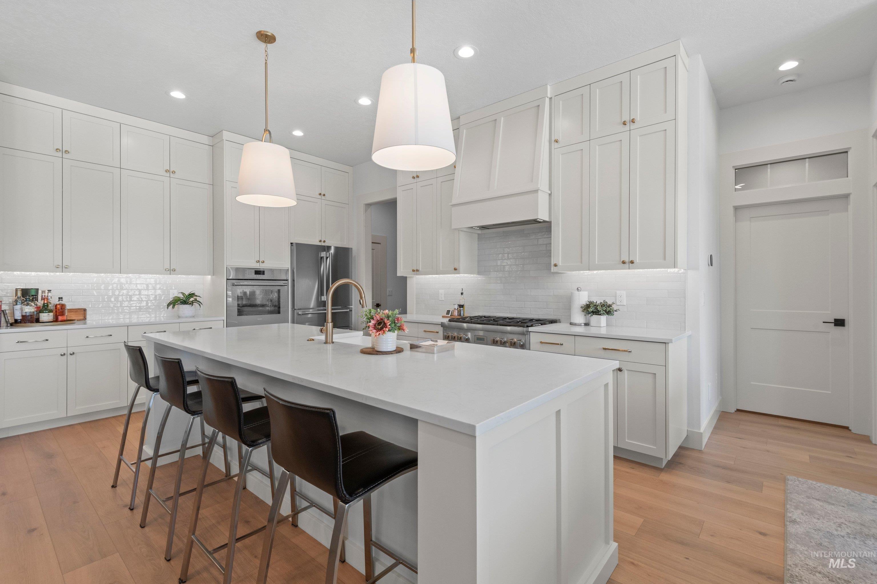 24990 Belgian Way Middleton, ID 83644 - Photo 6 of 50 Spacious kitchen featuring a large central island with seating, extensive white cabinetry, light wood-finish flooring, recessed lighting, and stainless steel appliances