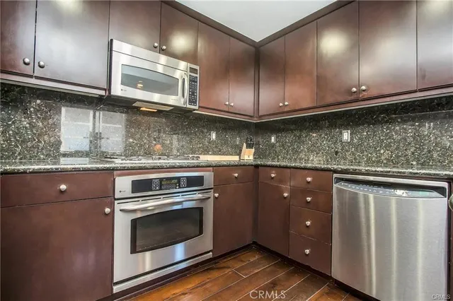 a kitchen with stainless steel appliances granite countertop wooden cabinets and a wooden floor
