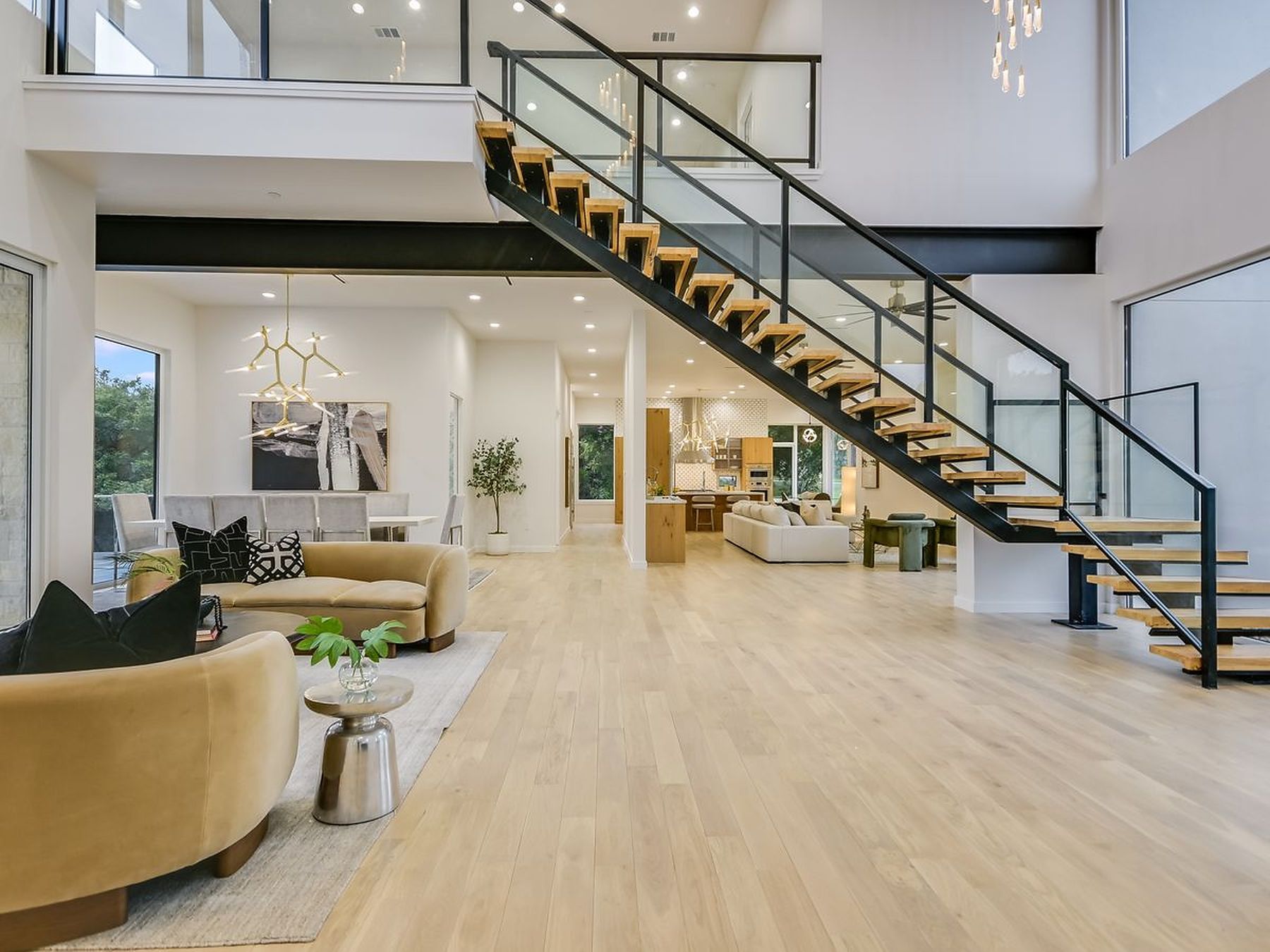 2476 Waymaker Way Austin, TX 78746 - Photo 14 of 31 A grand floating staircase with sleek glass railings anchors this open-concept living space, showcasing light hardwood floors and high ceilings.