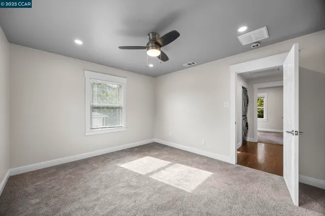 an empty room with ceiling fan and windows