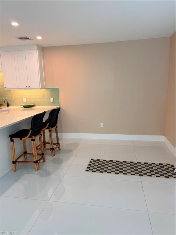 1575 Curlew Avenue, Unit 1 Naples, FL 34102 - Photo 20 of 35 Kitchen with a breakfast bar, decorative backsplash, white cabinets, light stone countertops, and light tile floors