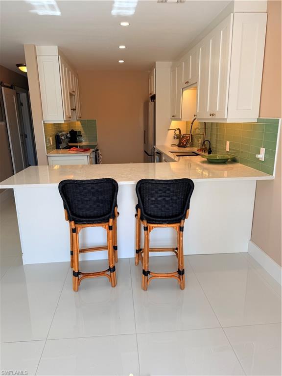 1575 Curlew Avenue, Unit 1 Naples, FL 34102 - Photo 21 of 35 Kitchen with tasteful backsplash, a kitchen breakfast bar, white cabinets, range, and a peninsula