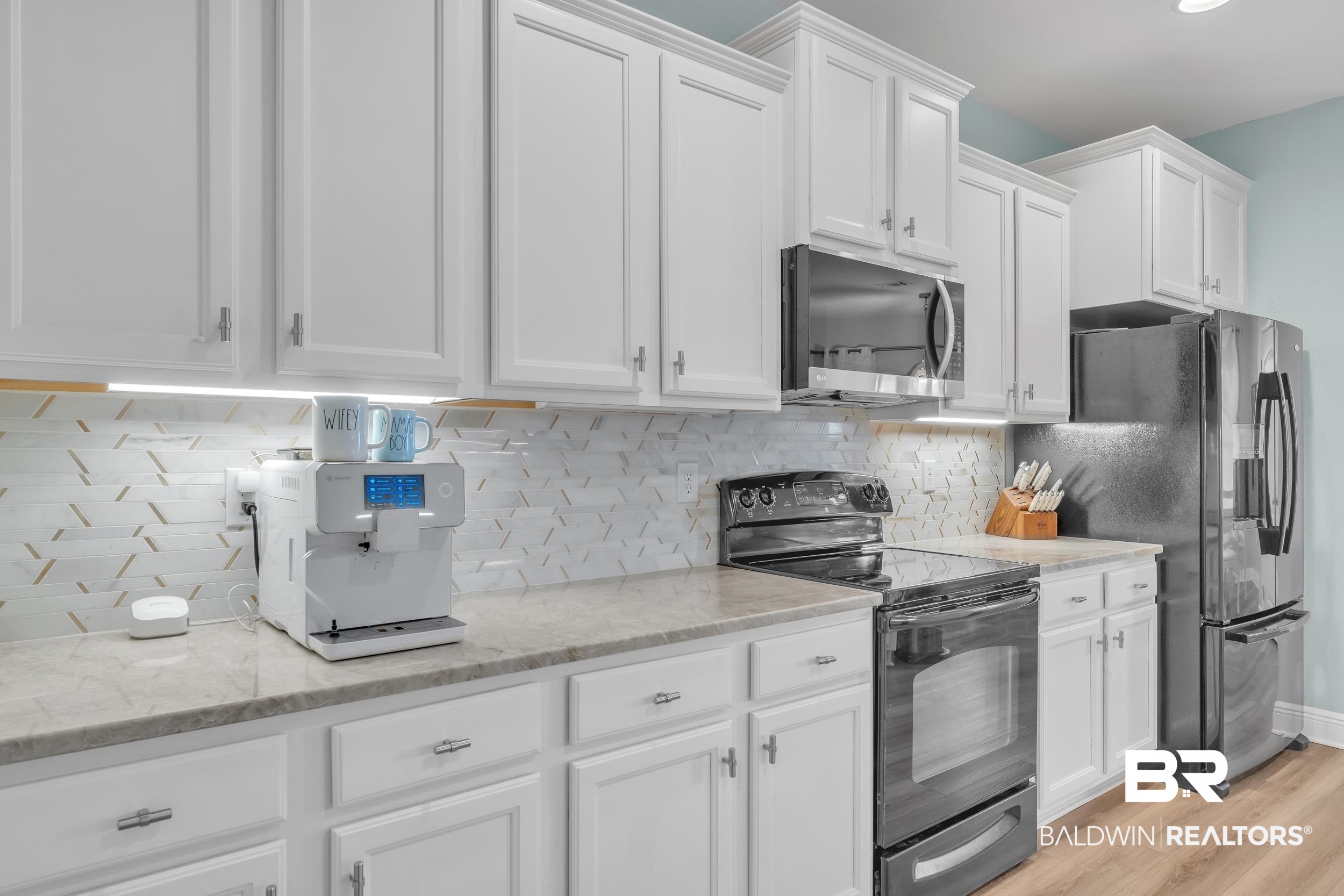 7109 Rocky Rd Loop Gulf Shores, AL 36542 - Photo 17 of 30 Kitchen with stainless steel appliances, light stone counters, backsplash, white cabinets, and light wood-style floors