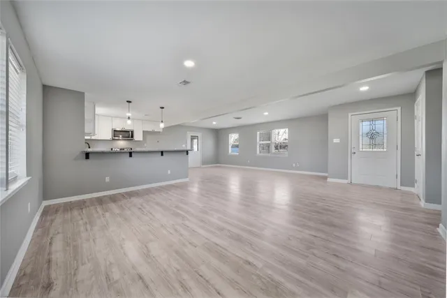 a view of a kitchen and an empty room with wooden floor and a window
