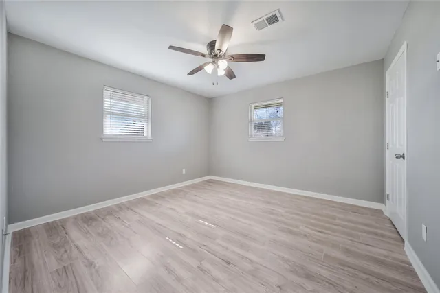 an empty room with wooden floor ceiling fan and windows