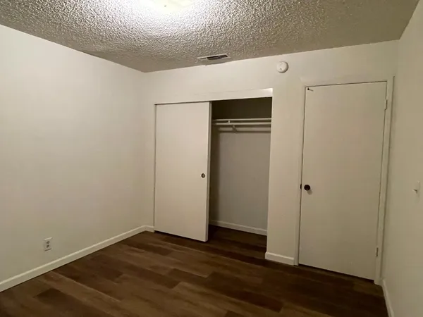 a view of an empty room with wooden floor and closet