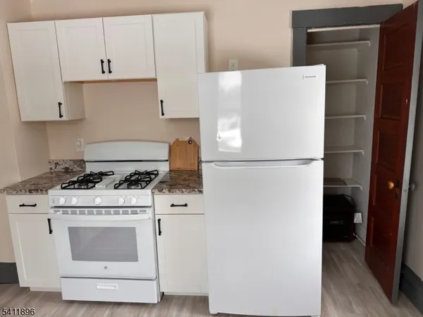 a white refrigerator freezer and a stove sitting inside of a kitchen with granite countertop white cabinets