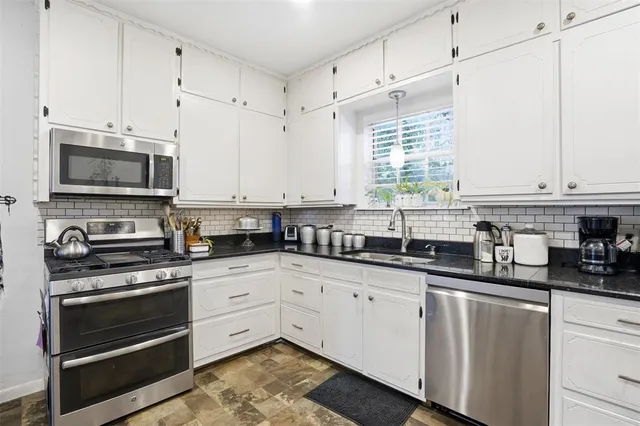 a kitchen with stainless steel appliances granite countertop a stove a sink and white cabinets