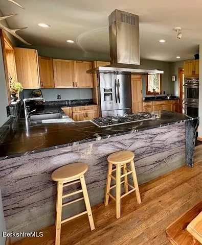 a kitchen with kitchen island a stove a sink a refrigerator wooden floor and a window