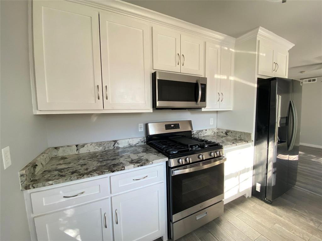 Kitchen featuring white shaker-style cabinetry, a built-in stainless steel microwave, a stainless steel range with a gas cooktop, and speckled stone countertops