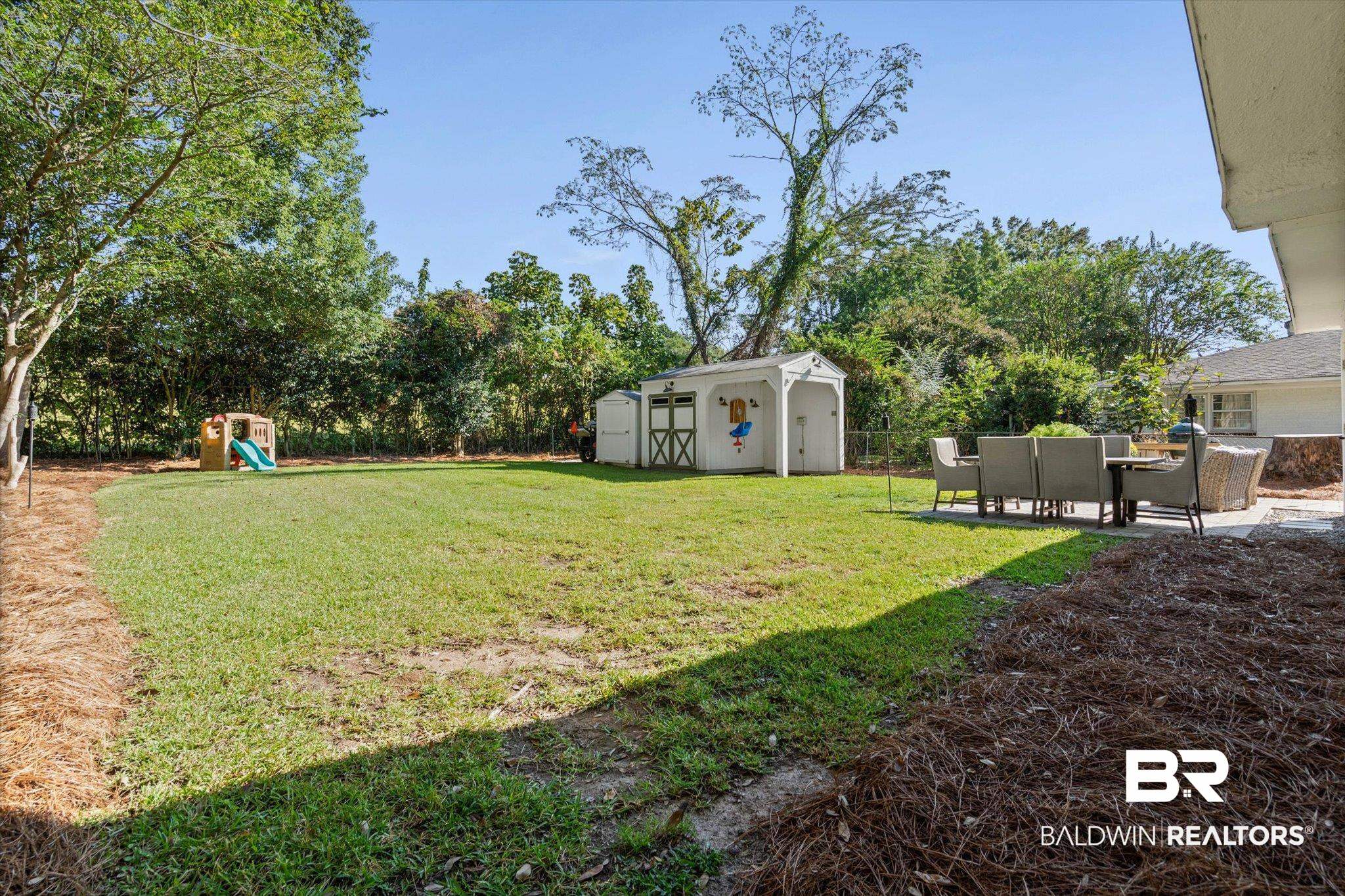 4310 The Cedars Avenue Mobile, AL 36608 - Photo 25 of 32 View of green lawn featuring a storage unit, a playground, a patio, and view of scattered trees