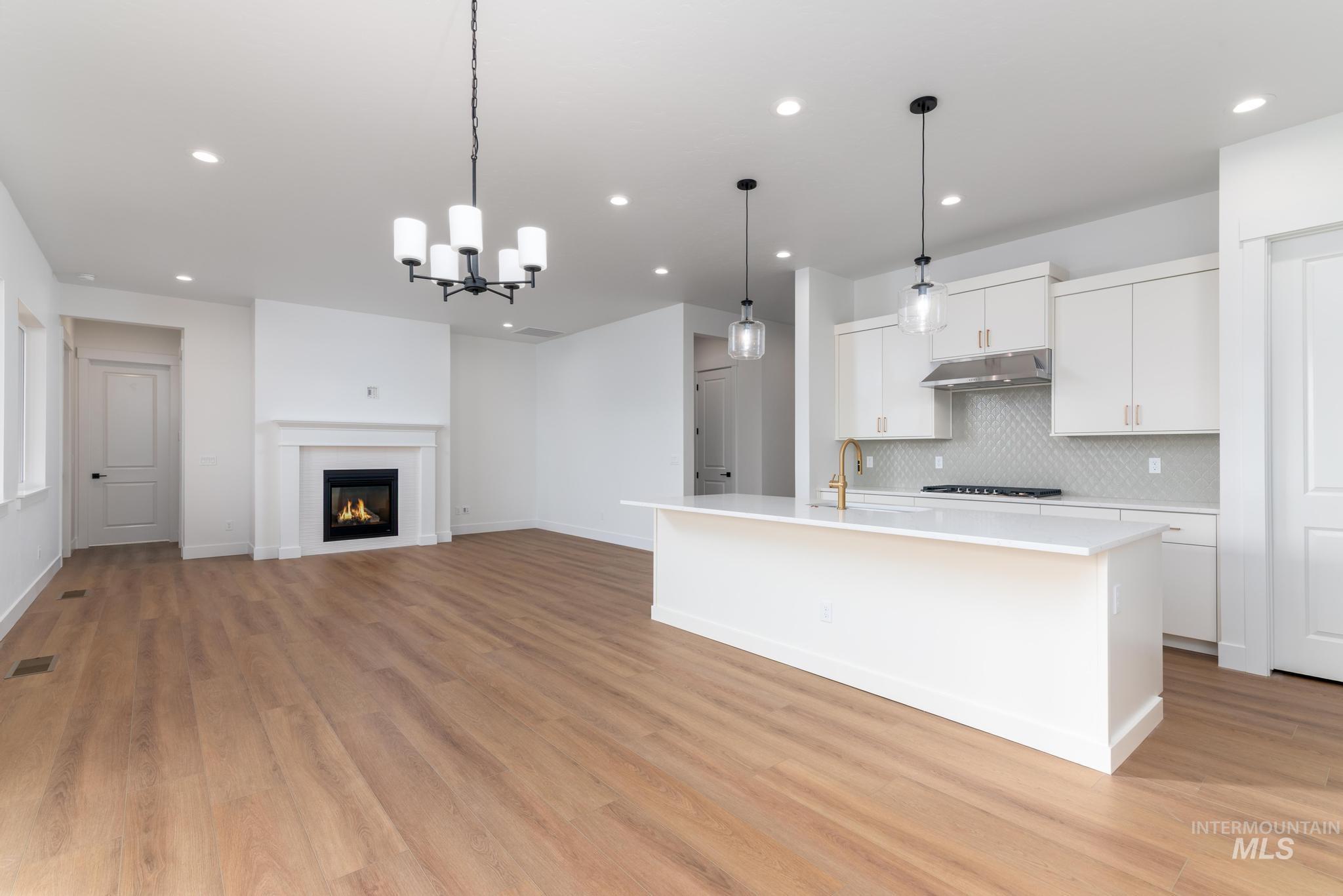 15142 Steel Cloud Avenue Caldwell, ID 83607 - Photo 34 of 34 Kitchen featuring white cabinets, a glass covered fireplace, an island with sink, open floor plan, and decorative backsplash
