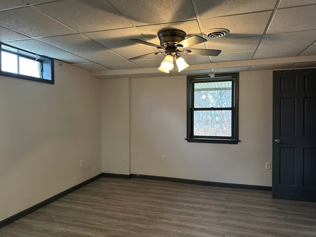 an empty room with wooden floor chandelier fan and windows