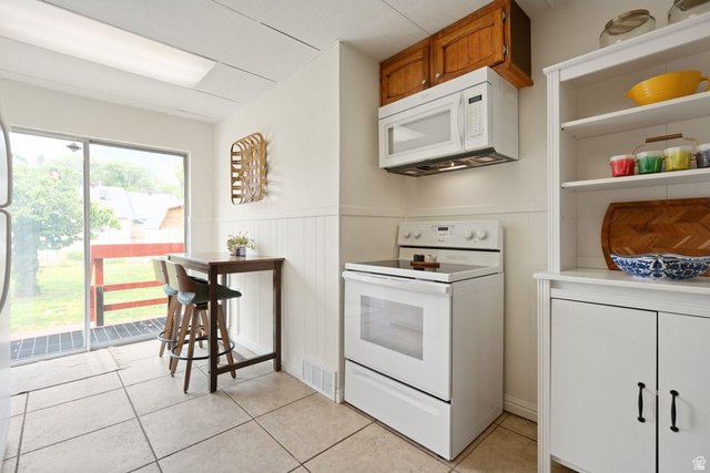 673 East 700 South Springville, UT 84663 - Photo 13 of 43 Kitchen featuring white appliances, upper wood cabinetry, a built-in microwave, white beadboard wainscoting, and tile flooring