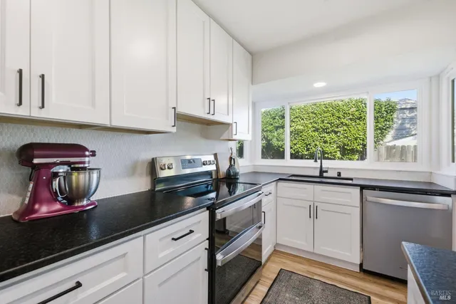 a kitchen with stainless steel appliances granite countertop white cabinets and a window