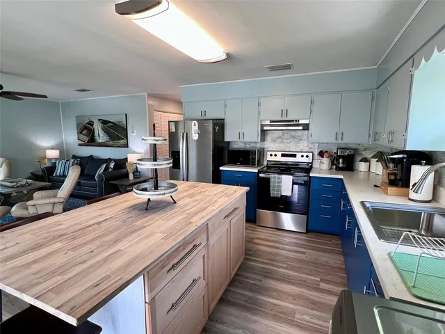 a large kitchen with stainless steel appliances wooden floor and a view of living room