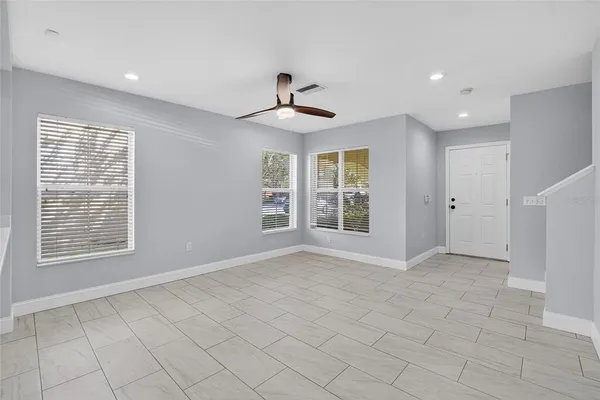 an empty room with chandelier fan and windows
