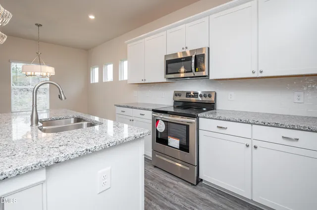 a kitchen with stainless steel appliances granite countertop a sink a stove and microwave with wooden floor