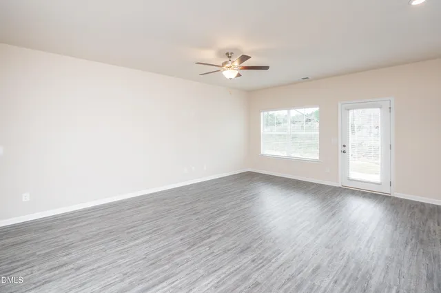 an empty room with wooden floor fan and windows