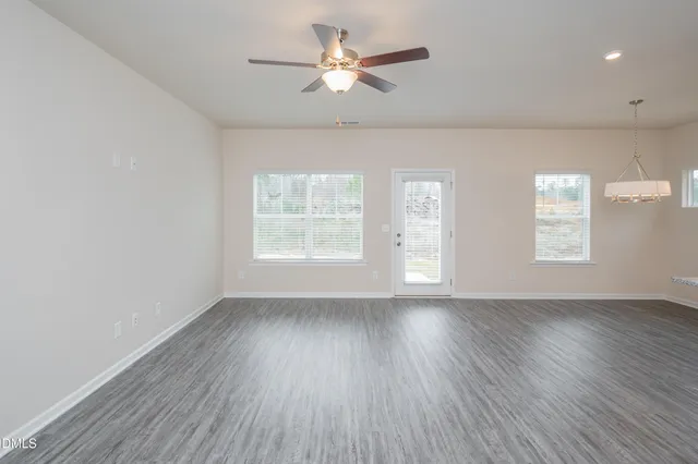 an empty room with wooden floor chandelier fan and windows