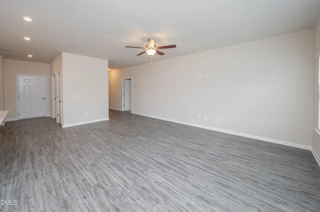 a view of a livingroom with wooden floor a ceiling fan and windows