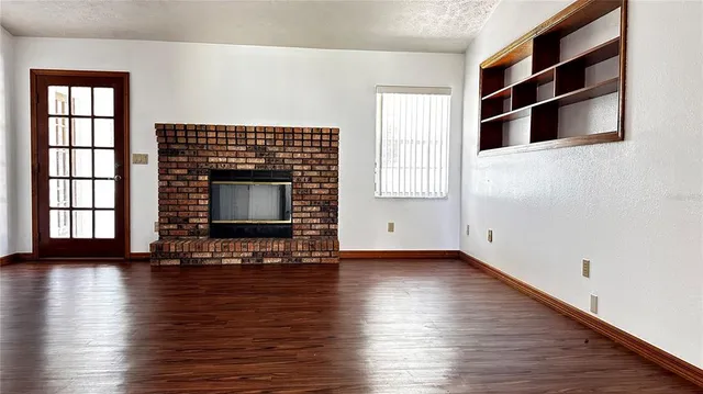 an empty room with wooden floor fireplace and windows