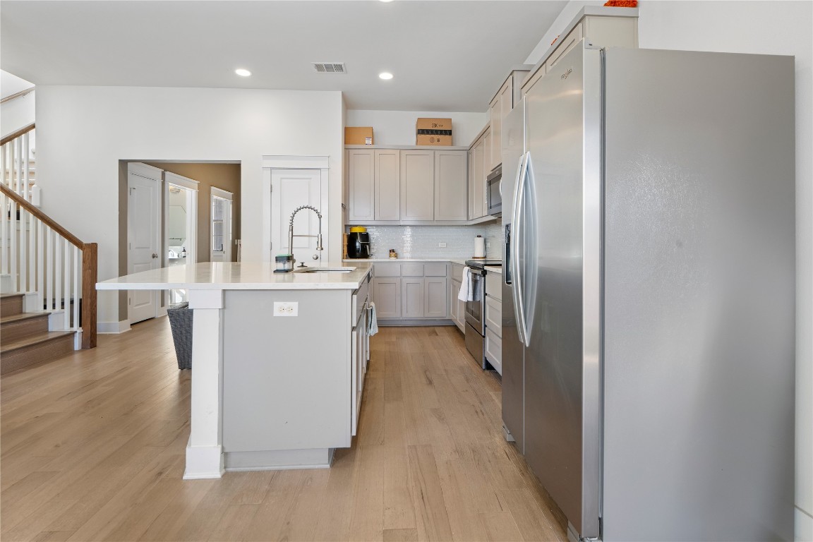 13001 Hymeadow Drive, Unit 31 Austin, TX 78729 - Photo 13 of 40 Kitchen featuring appliances with stainless steel finishes, a kitchen island with sink, light wood-style floors, light stone counters, and recessed lighting