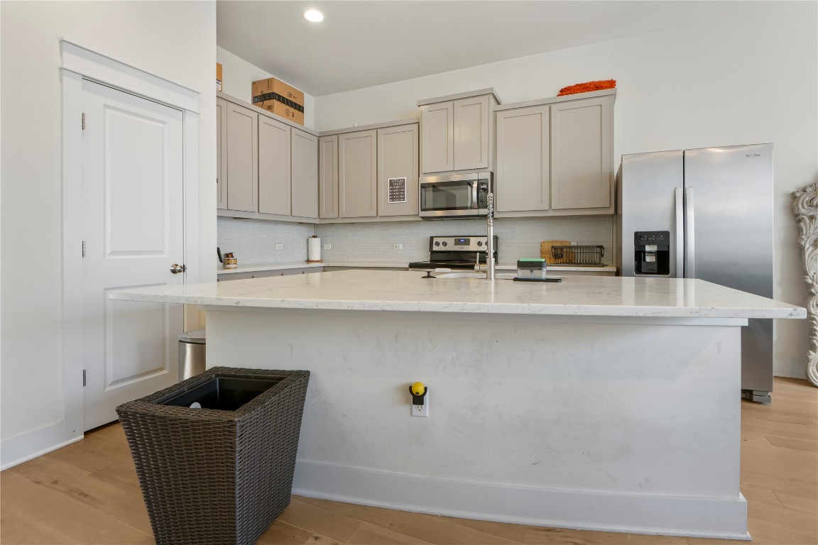 13001 Hymeadow Drive, Unit 31 Austin, TX 78729 - Photo 14 of 40 Kitchen with gray cabinetry, appliances with stainless steel finishes, light stone countertops, decorative backsplash, and light wood finished floors