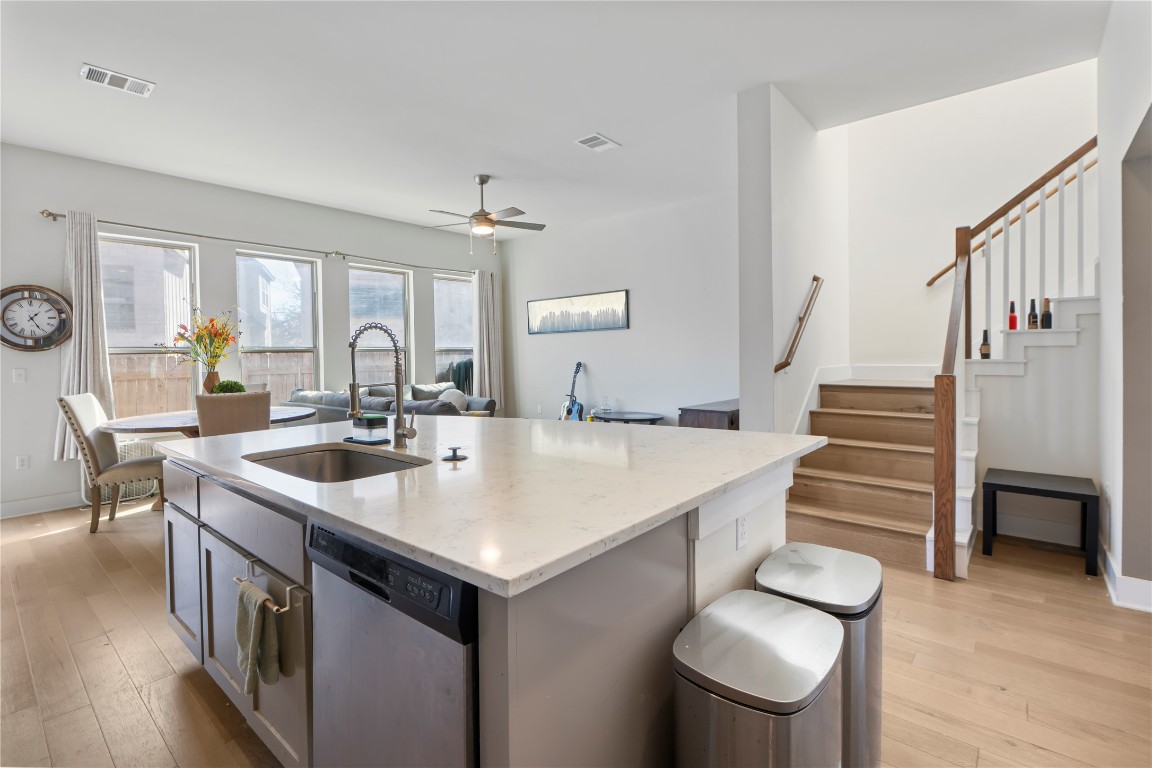 13001 Hymeadow Drive, Unit 31 Austin, TX 78729 - Photo 15 of 40 Kitchen featuring stainless steel dishwasher, a ceiling fan, light wood-style floors, a center island with sink, and light stone countertops