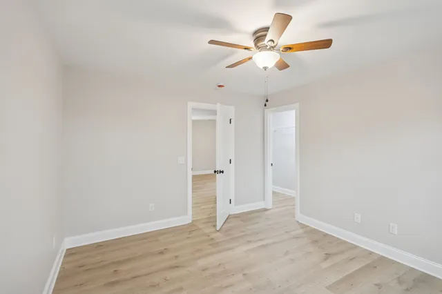 an empty room with wooden floor ceiling fan and windows