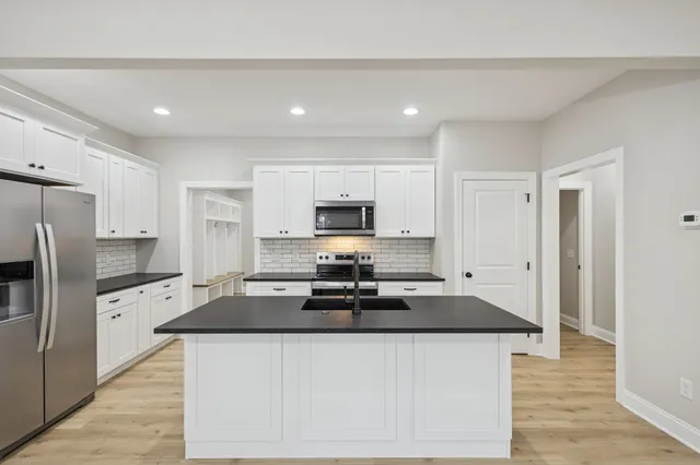 a kitchen with stainless steel appliances granite countertop a stove a sink a refrigerator and white cabinets