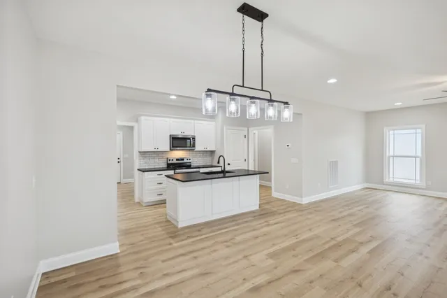 a kitchen with stainless steel appliances granite countertop a sink a stove a refrigerator and white cabinets