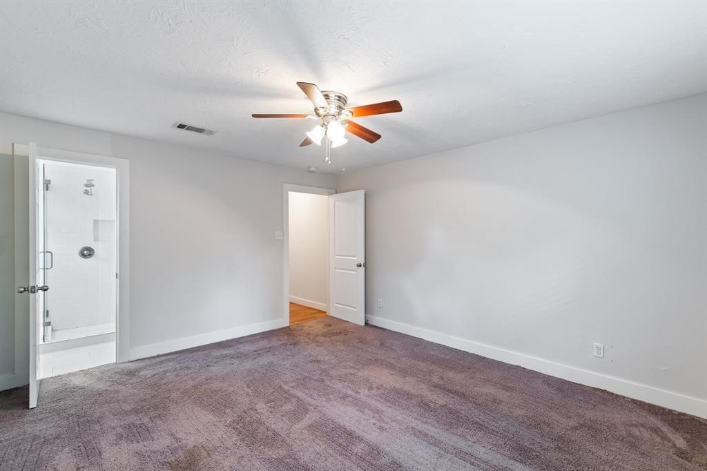 1305 Idylwild Street Houston, TX 77009 - Photo 22 of 31 This photo shows a spacious bedroom with fresh neutral walls, a ceiling fan, and dark carpeting. It features an en suite bathroom with a glass door shower, offering convenience and comfort.