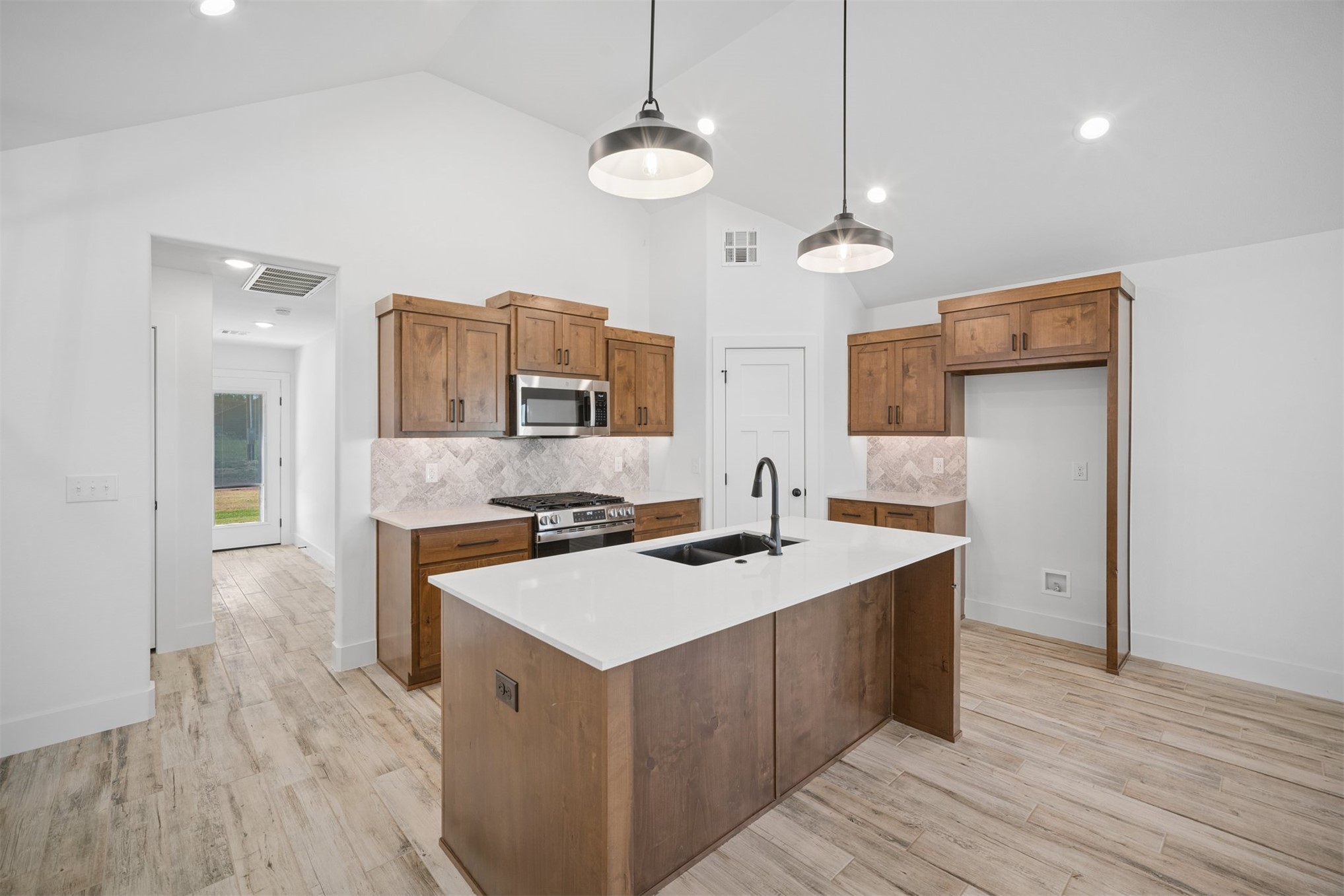 25036 South 4205 Road Inola, OK 74036 - Photo 9 of 30 Vaulted ceiling kitchen featuring wood-finish cabinetry, a large kitchen island with a dark sink, stainless steel appliances, and wood-finish flooring