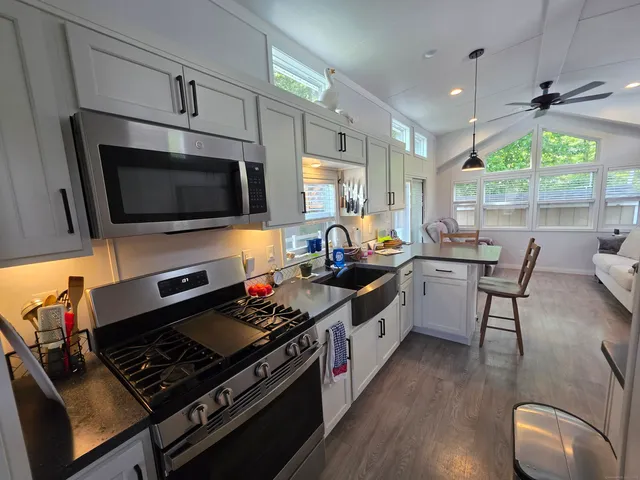 a kitchen with stainless steel appliances a stove a sink dishwasher and a microwave oven with wooden floor