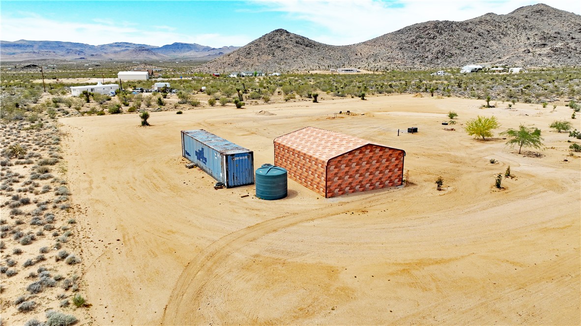5649 Davis Road Golden Valley, AZ 86413 - Photo 1 of 24 Expansive desert property featuring a metal storage building with a patterned exterior, a blue shipping container, and a green water storage tank