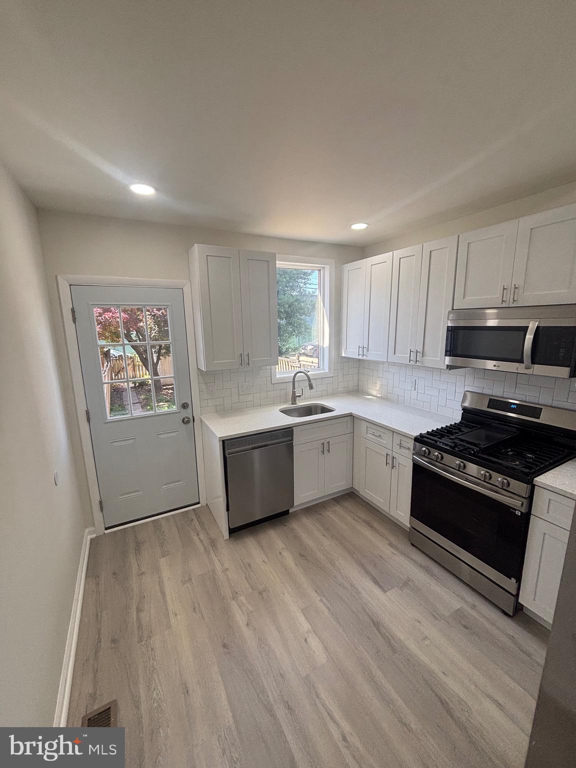 6769 Woodley Road Baltimore, MD 21222 - Photo 7 of 27 a large kitchen with a stove a sink dishwasher and a stove with wooden floor