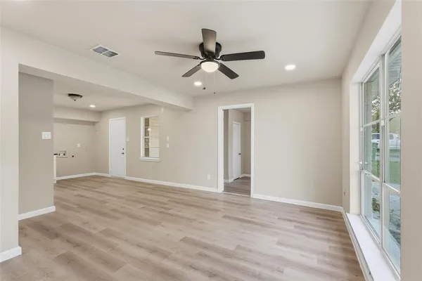a view of an empty room and window a ceiling fan and wooden floor
