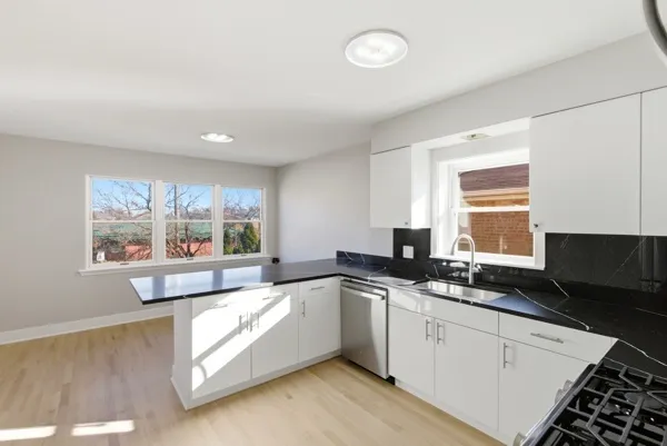 a large white kitchen with granite countertop a stove a sink and white cabinets with wooden floor