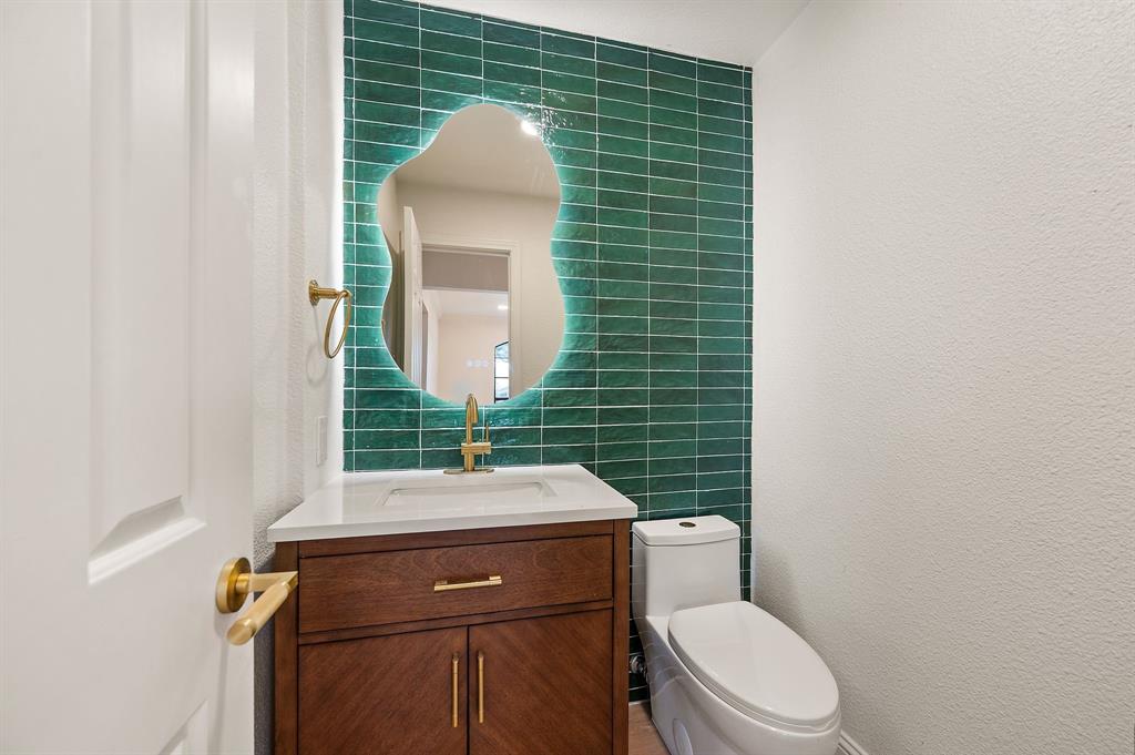 6403 Genstar Lane Dallas, TX 75252 - Photo 14 of 34 Accent wall with green subway tile, modern illuminated mirror, wood-finish vanity with white countertop, gold-tone faucet, and white commode