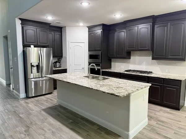 a kitchen with stainless steel appliances kitchen island granite countertop a refrigerator a sink and wooden cabinets