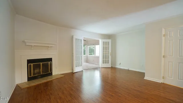 a view of an empty room with wooden floor fireplace and a window