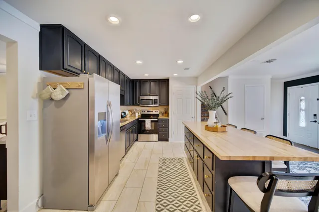 a kitchen with stainless steel appliances a refrigerator a sink dishwasher a stove top oven a dining table and chairs with wooden floor