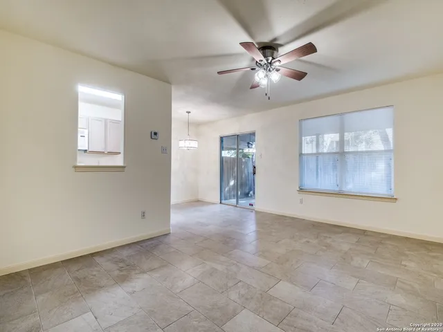 a view of an empty room with chandelier fan and windows
