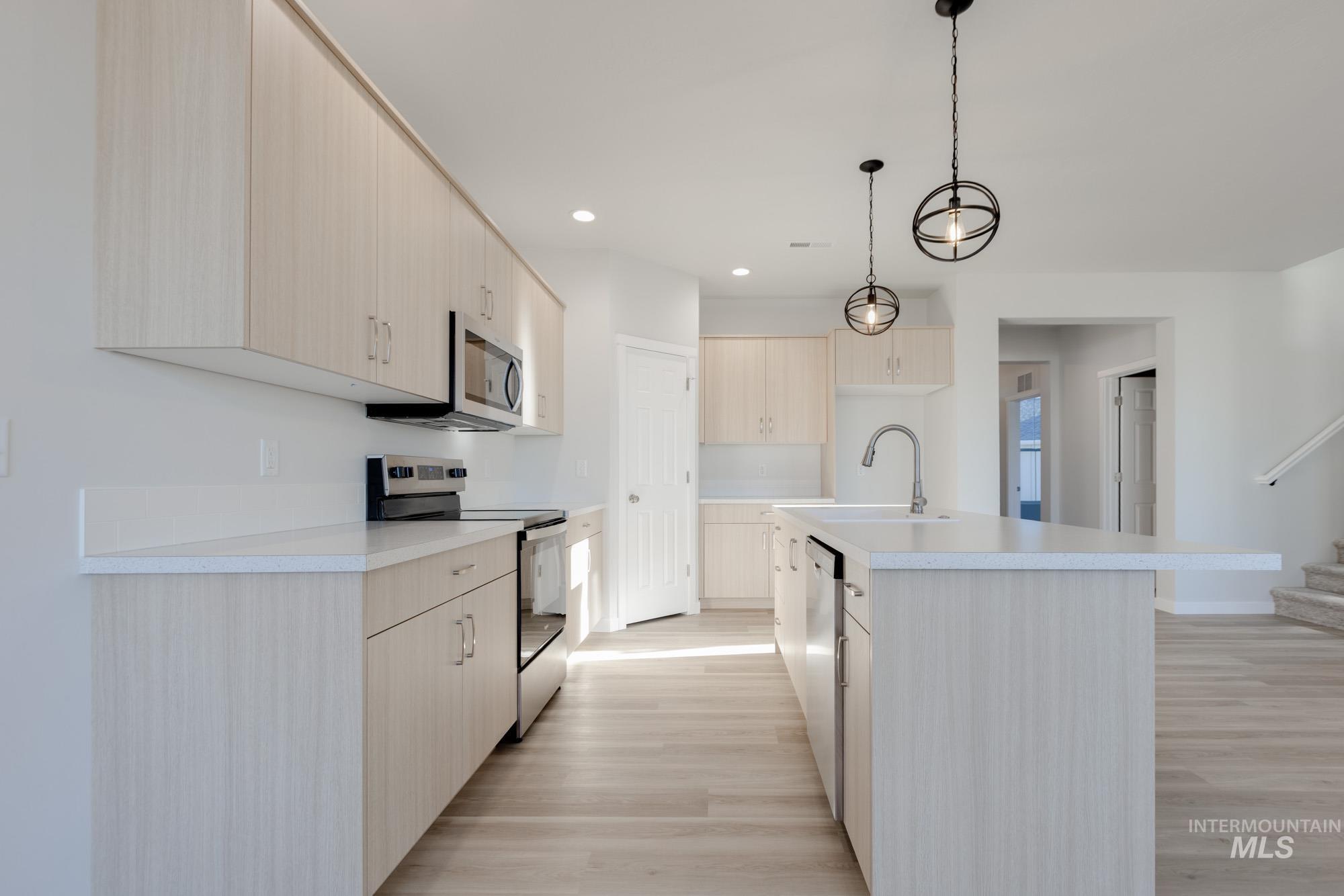 1639 Celina Street Middleton, ID 83644 - Photo 3 of 19 Modern kitchen featuring light wood-finish cabinetry, stainless steel appliances, a center island with a sink and pendant lighting, white countertops, and wood-finish flooring